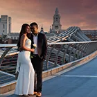 Couple photoshoot on the Millennium Bridge; the man is embracing the woman holding a white rose, with St. Paul's Cathedral in the background.