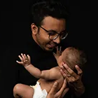 Father lifting his newborn baby up and smiling against a black background.