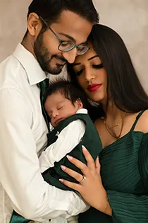 Intimate family photo of the parents embracing while the father holds their sleeping newborn, a beautiful shot from their family photoshoot.