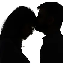 Dramatic silhouette maternity photoshoot and maternity photo showing father kissing mother's forehead.