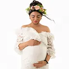 Solo maternity photoshoot in white lace dress and flower crown; elegant maternity photography.