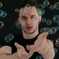 Professional modeling portfolio shot of a male model with floating bubbles against a black background.