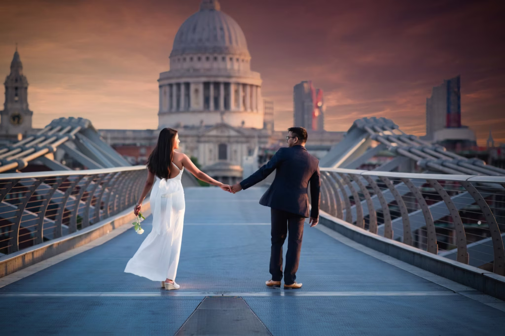 Wide shot of couple walking away toward St. Paul's Cathedral on bridge holding hands looking back at one another with woman carrying single white rose, steel bridge cables creating leading lines - proposal photographer london
