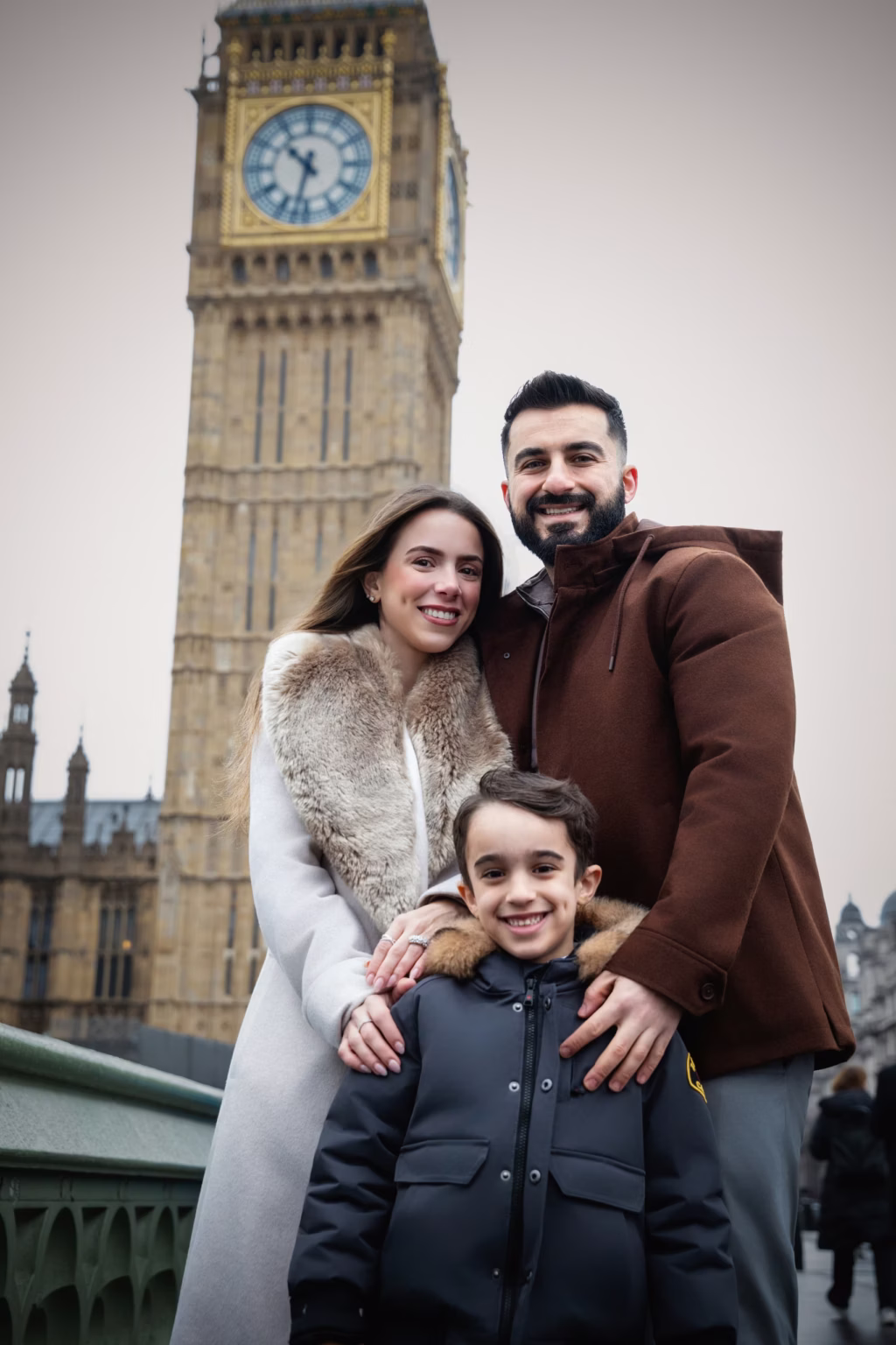 Family of three-mother, father, and young son-pose in front of Big Ben in London, wearing warm winter coats, overcast sky typical of London afternoon - family photographer, Big Ben winter family