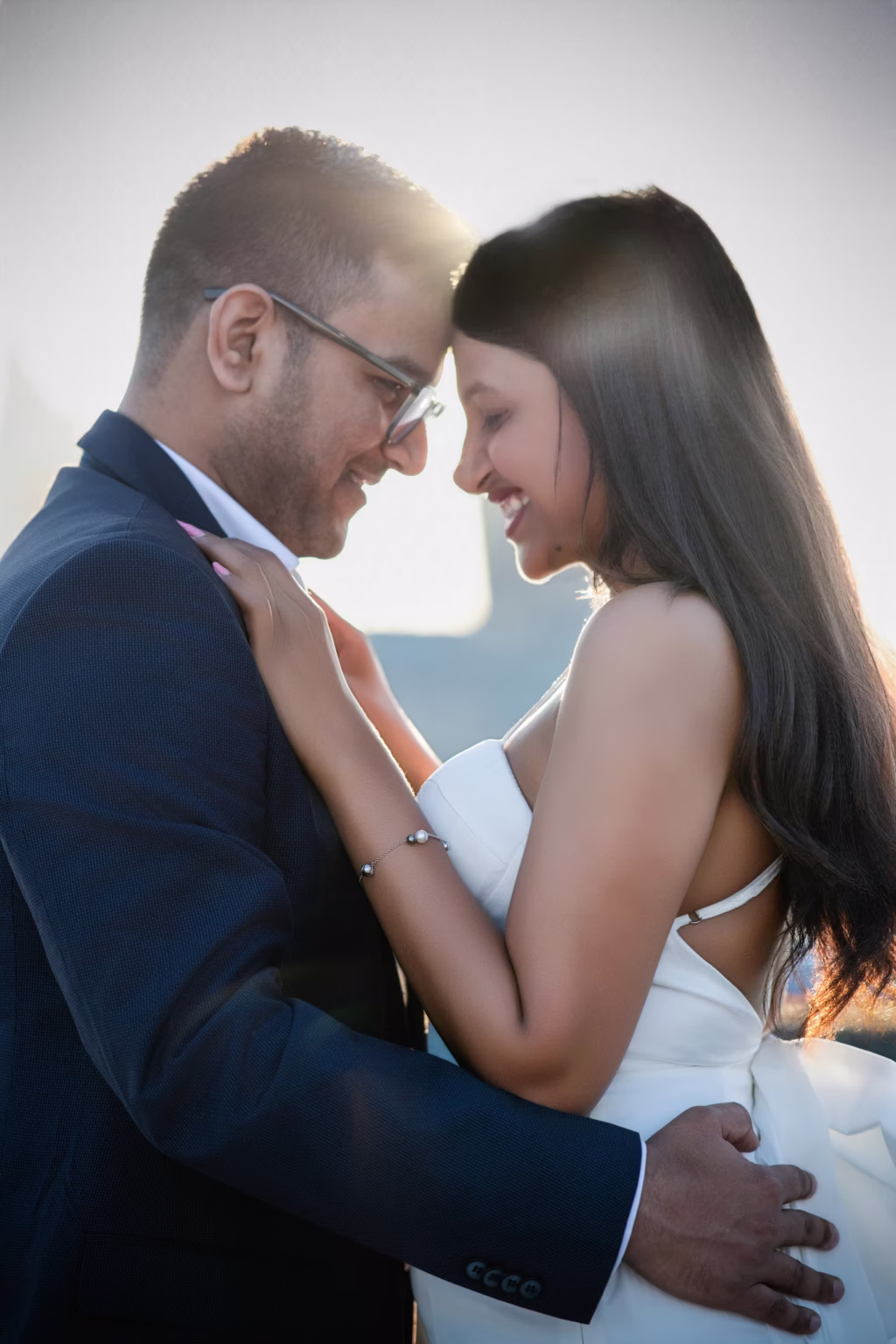 Warm intimate close-up of couple facing each other with foreheads touching and eyes closed, man's hand on woman's waist and woman's hand on his shoulder with soft lens flare from setting sun - engagement photographer london