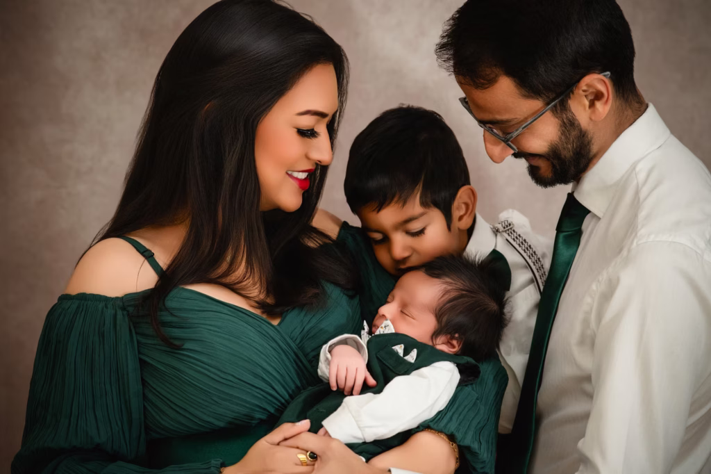Tender profile shot of mother father and older son all looking down lovingly at sleeping newborn cradled in mother's arms - family photo studio