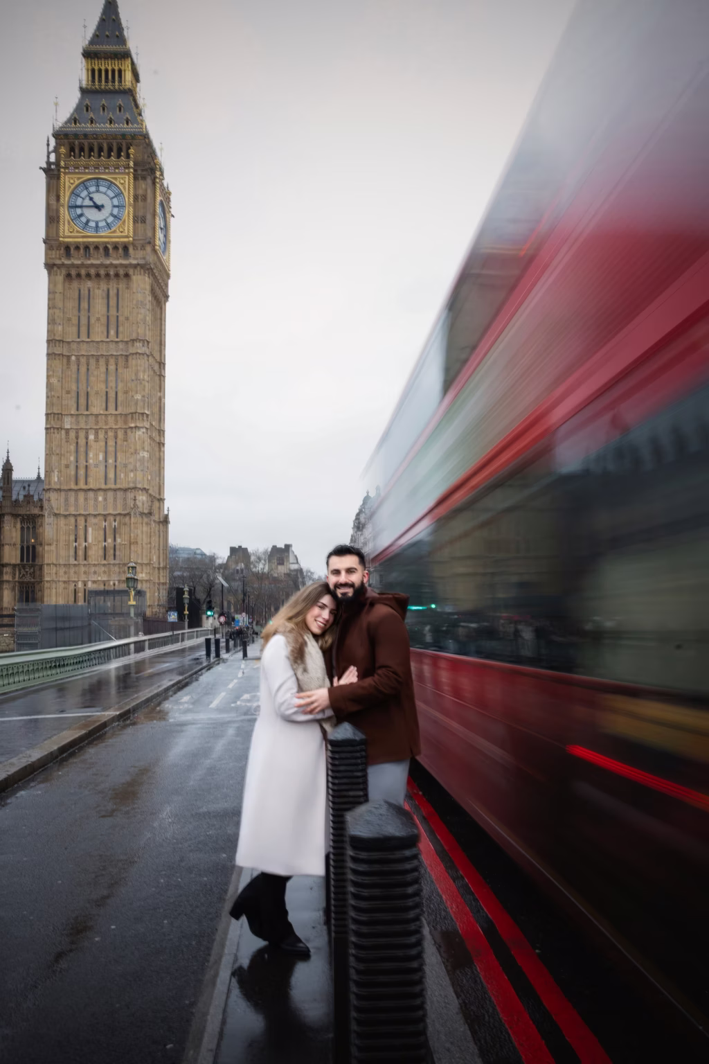 Long-exposure shot on Westminster Bridge couple embracing while red double-decker bus blurred into streak of motion behind them Big Ben stands tall in background