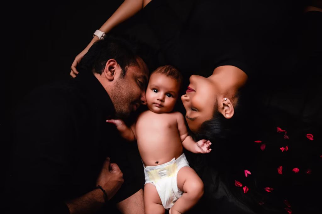 With parents and baby on black background with red rose petals - family photography studio