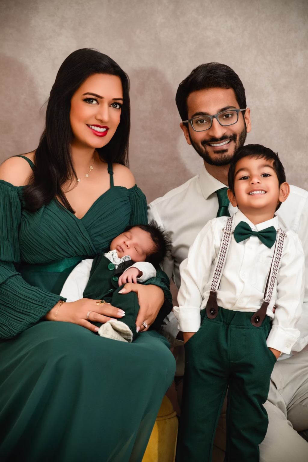 Of four in coordinated studio portrait mother father older son smile at camera while mother holds sleeping newborn all dressed in green and white - studio photography family