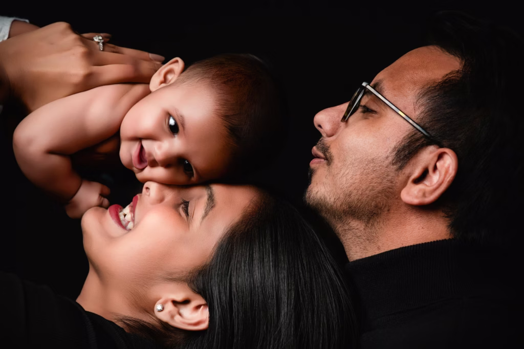 London family portraits of mother and father laughing with shirtless baby on black background