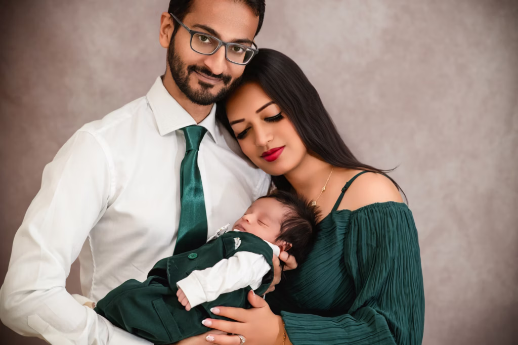 Of mother and father cradling sleeping newborn mother leans head against father both wearing forest green and white against textured grey background - family photo studio