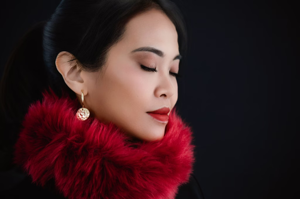 London Fashion Photo Studio - Woman close-up high-contrast portrait black background eyes closed red faux-fur collar gold coin-style earring bold red lip makeup