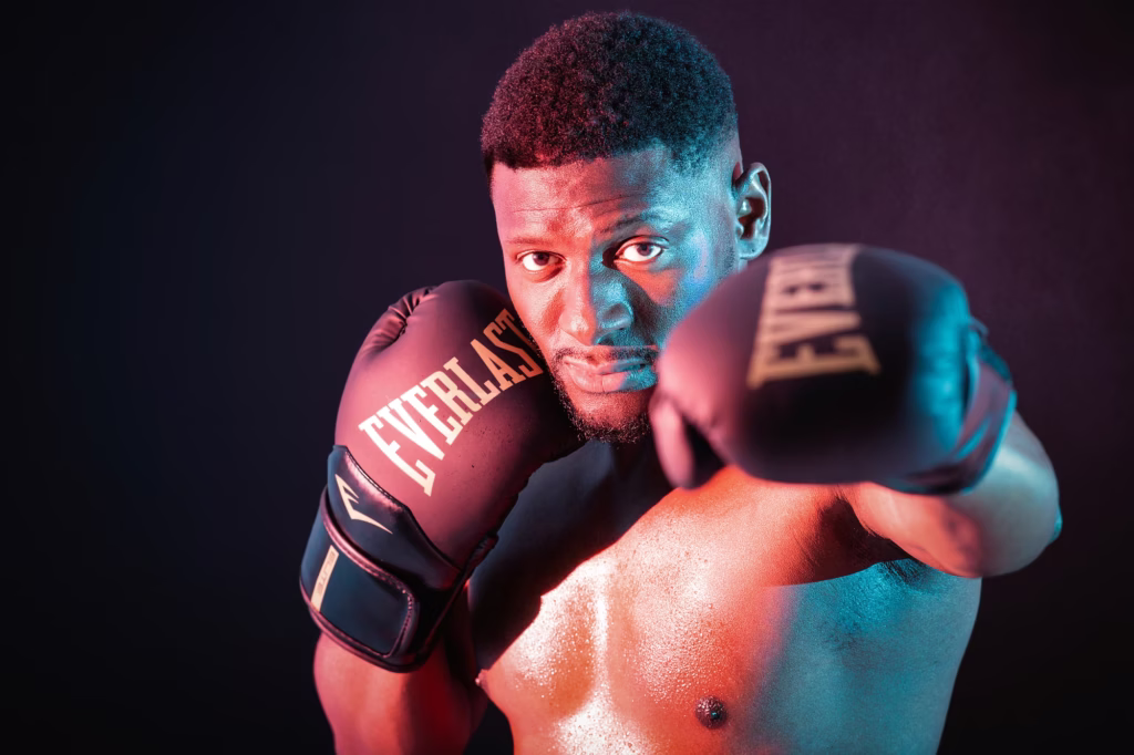 London Fashion Photographers - Powerful athletic portrait shirtless man black Everlast boxing gloves defensive stance intense camera gaze highly stylized orange teal lighting highlights skin