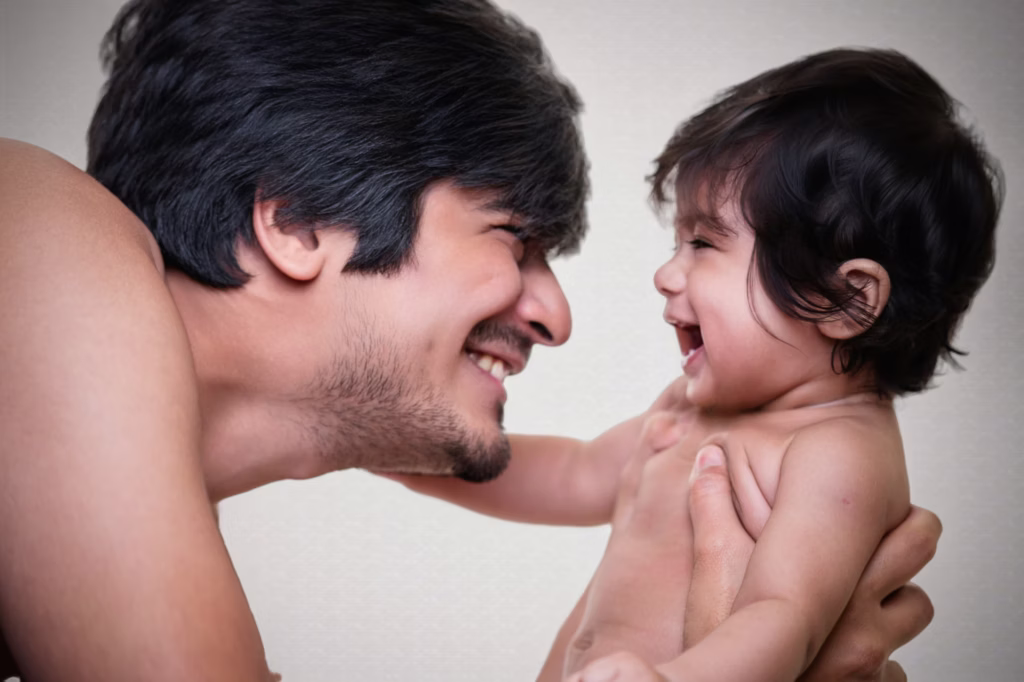 Intimate close-up portrait of father and baby, father looking at infant with broad loving smile, baby laughing back at him, tightly framed to capture emotional connection - newborn photos, father baby laugh