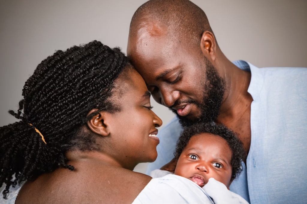 london newborn photography shoot Family portrait of two parents and baby leaning foreheads together tenderly with infant looking at camera with wide eyes