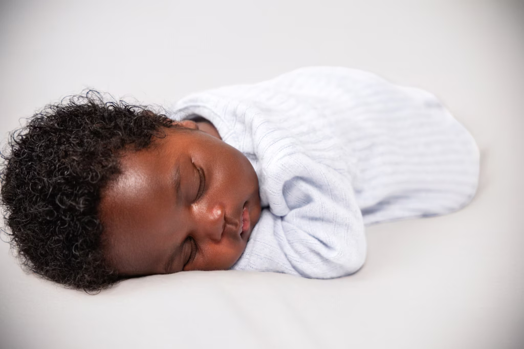 A newborn sleeping in a white swaddle