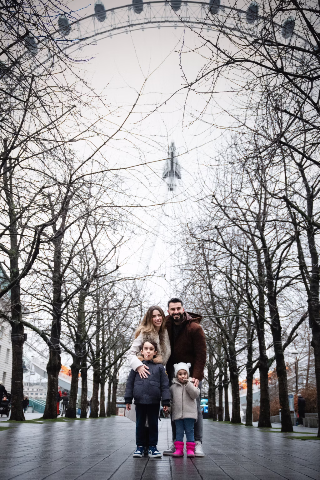 London photography of family in tree-lined walkway with London Eye visible and winter coats