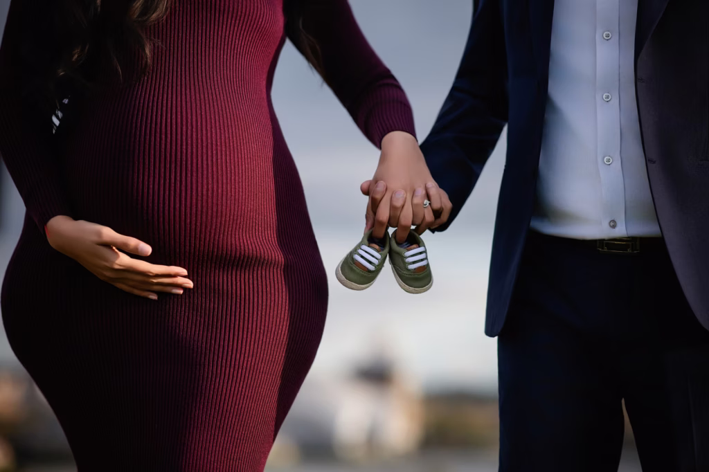 Close-up of hands over the bump holding baby shoes outdoors