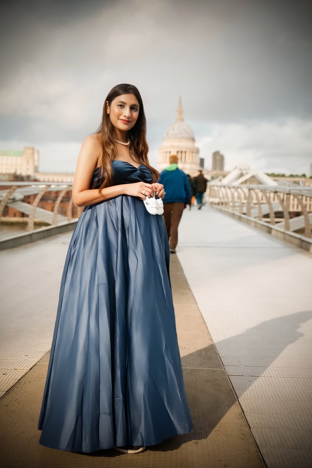 Expectant mother in a blue gown by a London river bridge