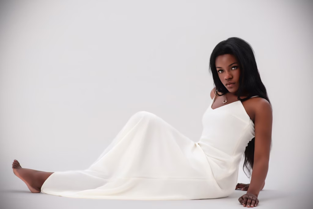 London Fashion And Photography - High-fashion studio shot woman sitting floor clean white background long elegant white spaghetti-strap gown barefoot direct confident gaze