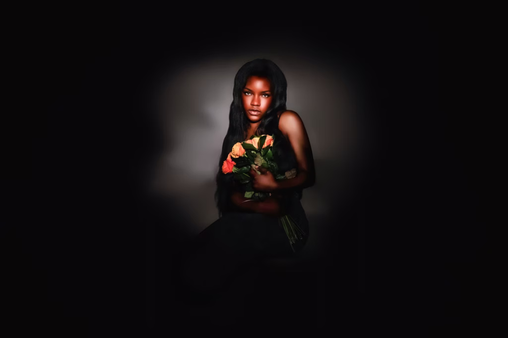 High-drama low-key portrait of woman sitting against black background in black lace dress holding orange roses with dramatic focused lighting - fashion photographer london