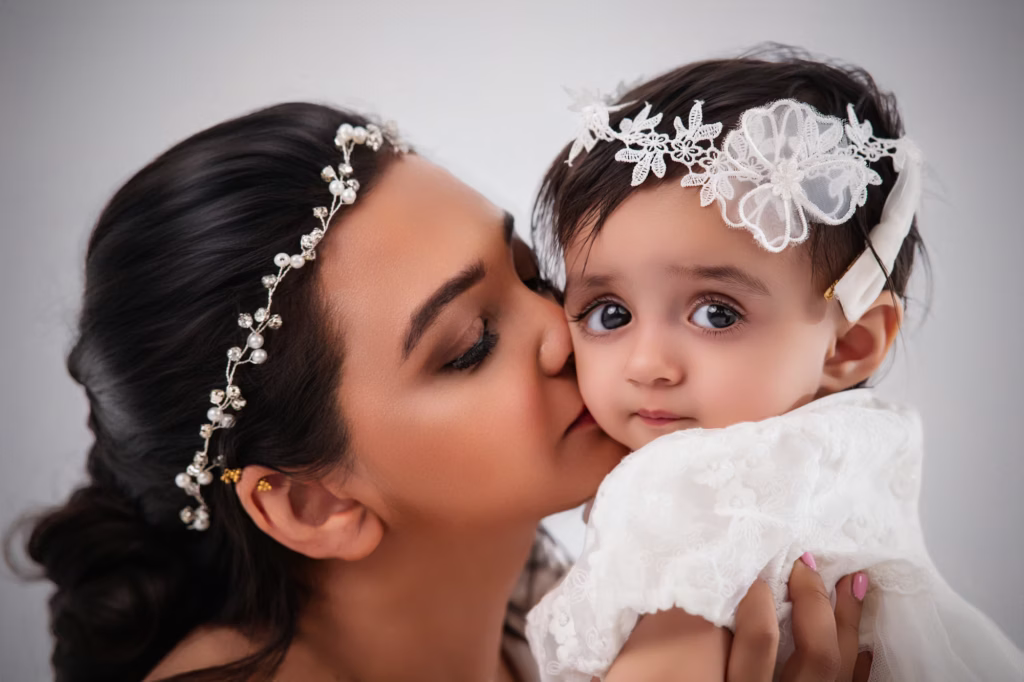 newborn photoshoot london Tender close-up of woman kissing toddler on cheek both wearing decorative floral pearl headpieces toddler looking at camera with large dark eyes